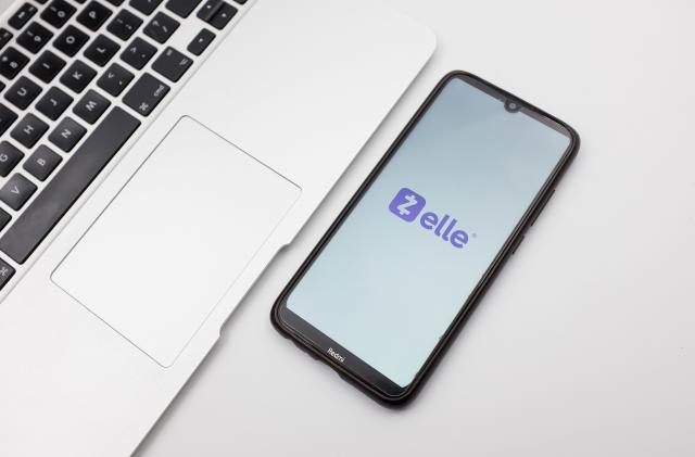 In this photo illustration a Zelle logo seen displayed on a smartphone screen on a desk next to a Macbook in Athens, Greece on September 29, 2022. (Photo Illustration by Nikolas Kokovlis/NurPhoto via Getty Images)