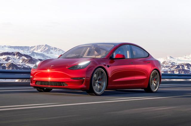 Marketing image for the Tesla Model 3. The red car drives on an open highway with snowy mountains in the background.