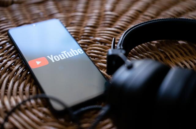 Headphones connected to a mobile phone with the logo of You tube on its screen. (Photo by Nikos Pekiaridis/NurPhoto via Getty Images)