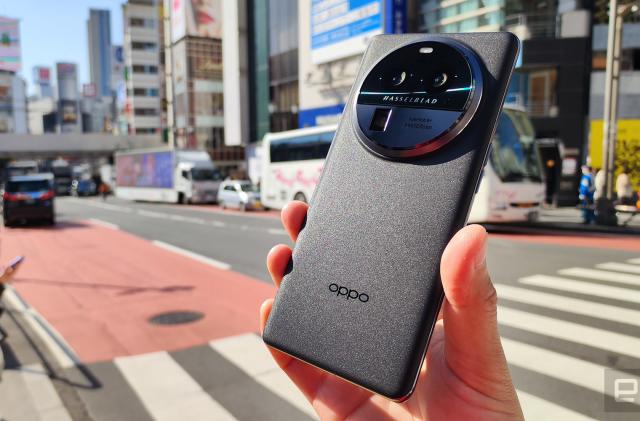 This image shows a hand holding the Oppo Find X6 Pro in front of a city street by a crosswalk.