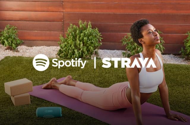 A person does yoga in an outdoor garden with the Spotify and Strava logos laid on top of her. 